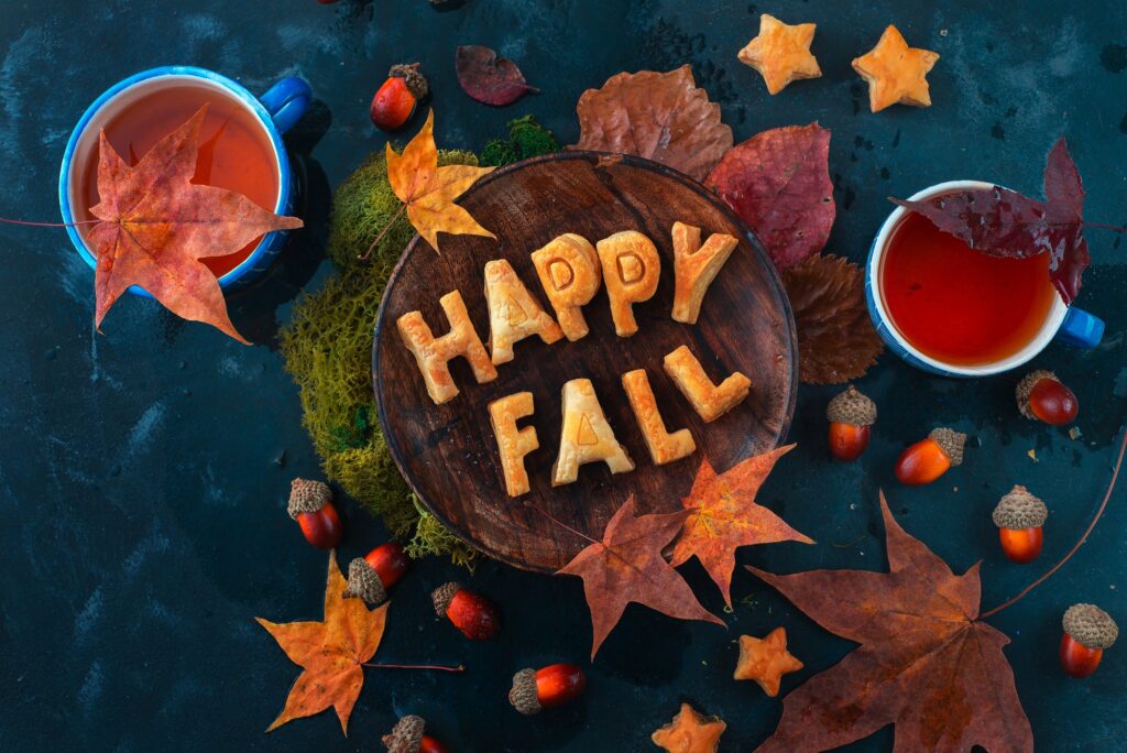Happy fall food lettering made with cookies. Autumn flat lay with tea, sweets and fallen leaves on a